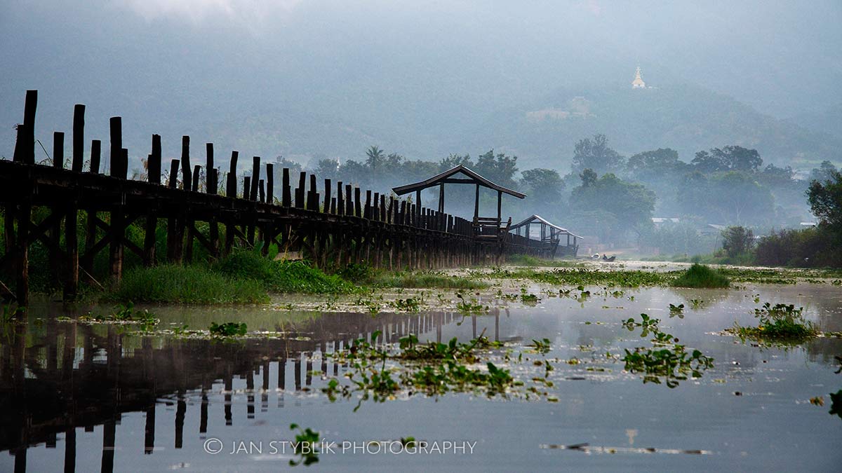Dřevěné molo na jezeře Inle v ranní mlze za úsvitu, s kopcem se stúpou v pozadí, Myanma